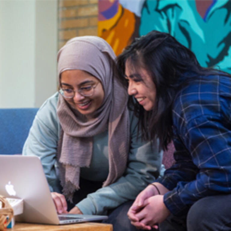 Two students smile while looking over a shared laptop within the Asian Pacific student center